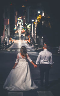 Rear view of couple walking on illuminated street at night