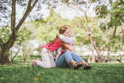 Rear view of woman sitting on grass against trees