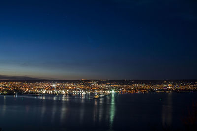 Illuminated city by sea against sky at night