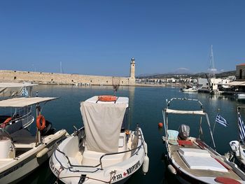 Boats moored at harbor against clear blue sky