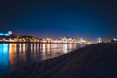 Illuminated buildings by river against sky at night