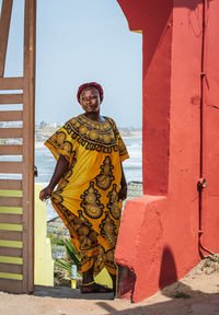 Africa woman wearing yellow suit stands at a gate with background over the city of accra in ghana