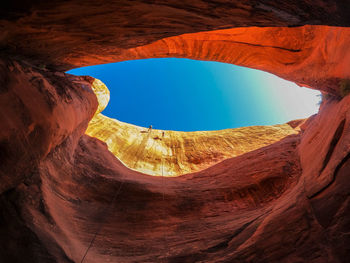 Low angle view of man climbing on rock against sky