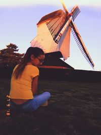 Woman sitting on field against sky during sunset