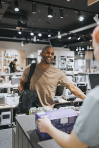 Smiling mature man talking with sales clerk at checkout counter in appliances store