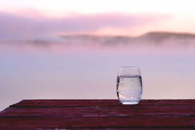 Close-up of glass on table against sea during sunset