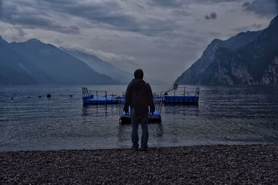 Rear view of man standing on lakeshore against mountains