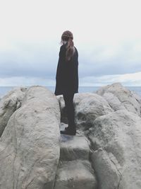 Low angle view of woman standing on rock against sea