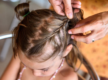 Cropped hands of mother braiding daughter hair