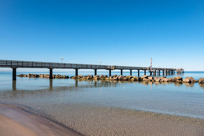 Pier over sea against clear blue sky