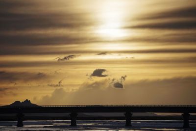 Silhouette bridge over sea against sky during sunset