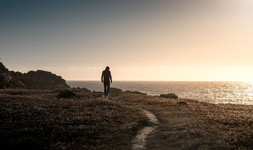 Rear view of man standing on cliff by sea during sunset