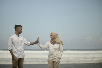 Full length of friends standing on beach against clear sky