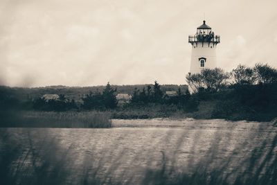 Lighthouse amidst trees and buildings against sky