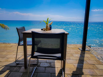 Deck chairs on table by sea against sky