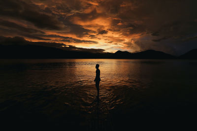 Silhouette man standing in sea against cloudy sky during sunset