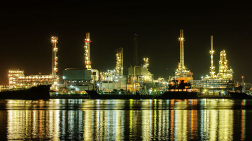 Illuminated factory by sea against sky at night