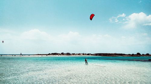 Person paragliding in sea against sky