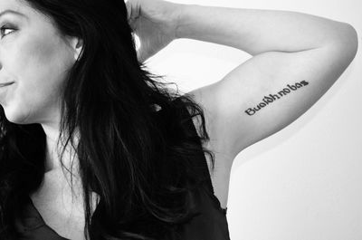 Cropped image of woman showing tattoo on her arm against wall