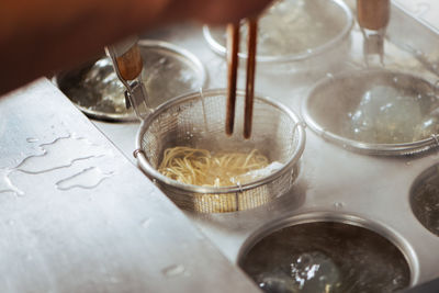 Cropped hand boiling noodles in container