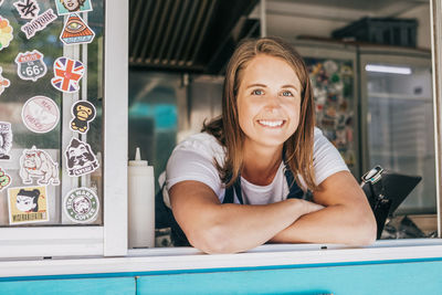 Portrait of smiling young female owner leaning on food truck window