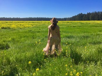 Rear view of woman standing on grassy field against clear sky