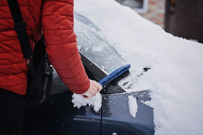 Man cleaning car from snow and ice with brush and scraper tool during snowfall. winter emergency