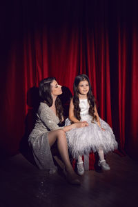 Beautiful young woman in a shiny dress is sitting with a daughter child on red gift boxes with bows 