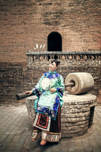 Smiling young woman with hand fan sitting outside historic building