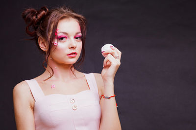 Beautiful young woman with make-up holding sweet food against gray background