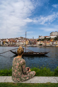 Rear view of woman sitting by river against sky