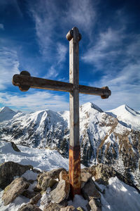 Cross on snow covered mountain against sky