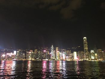 Illuminated city by river against sky at night