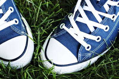 Low section of person wearing blue canvas shoes on grass