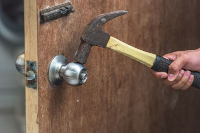 Cropped hand of man breaking doorknob with hammer