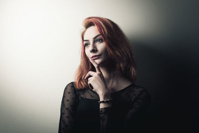 Beautiful young woman looking away while standing against wall