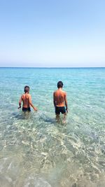 Rear view of friends walking on sea shore against clear sky