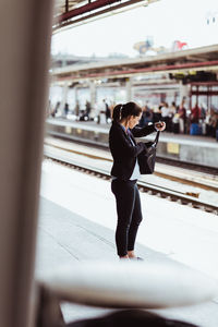 Female executive searching in bag while standing at railroad station