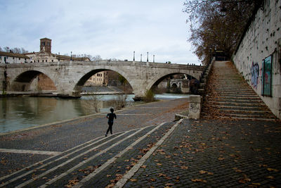 Rear view of woman jogging by river against arch bridge