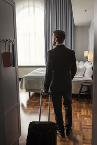 Rear view of businessman with luggage standing in hotel room