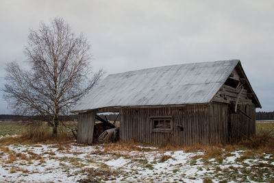 An old barn house stands on the winter fields. there is only a little snow on the ground.