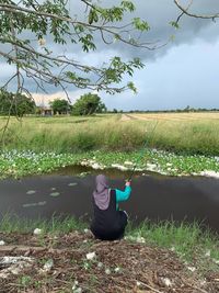 Man sitting on field by land against sky