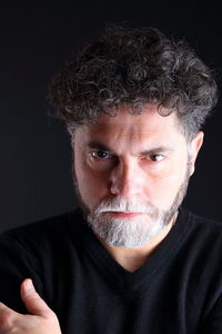 Close-up portrait of serious man with beard against black background