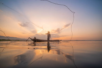 Silhouette man fishing in sea against sky during sunset