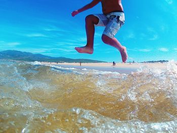 Low section of man jumping in sea against sky