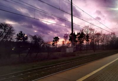 Railroad tracks by trees against sky during sunset