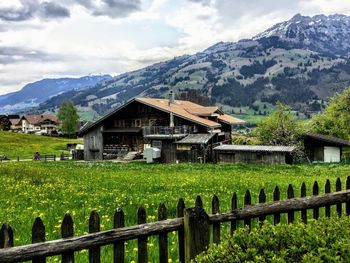 Scenic view of field by houses and mountains against sky