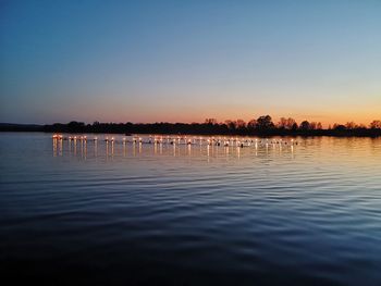 Scenic view of lake with swimmers and torches against clear sky during sunset