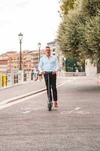 Young businessman in a suit riding an electric scooter while commuting to work in city. 