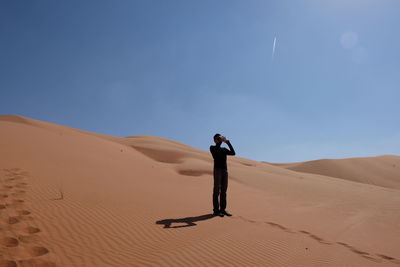 Man photographing while standing on sand against clear sky